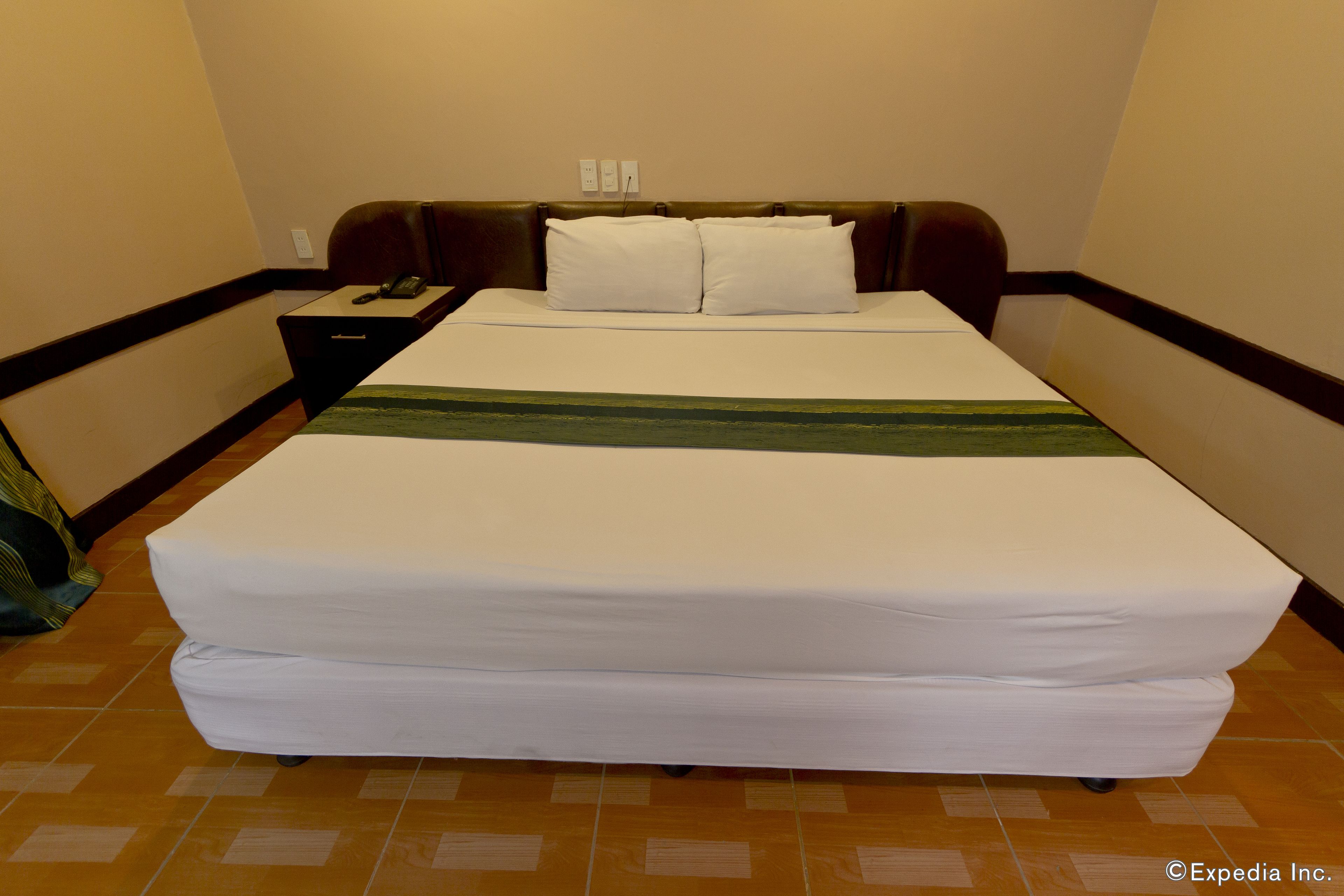 Une chambre d’hôtel avec un grand lit, une table de chevet avec un téléphone et une petite table de nuit.