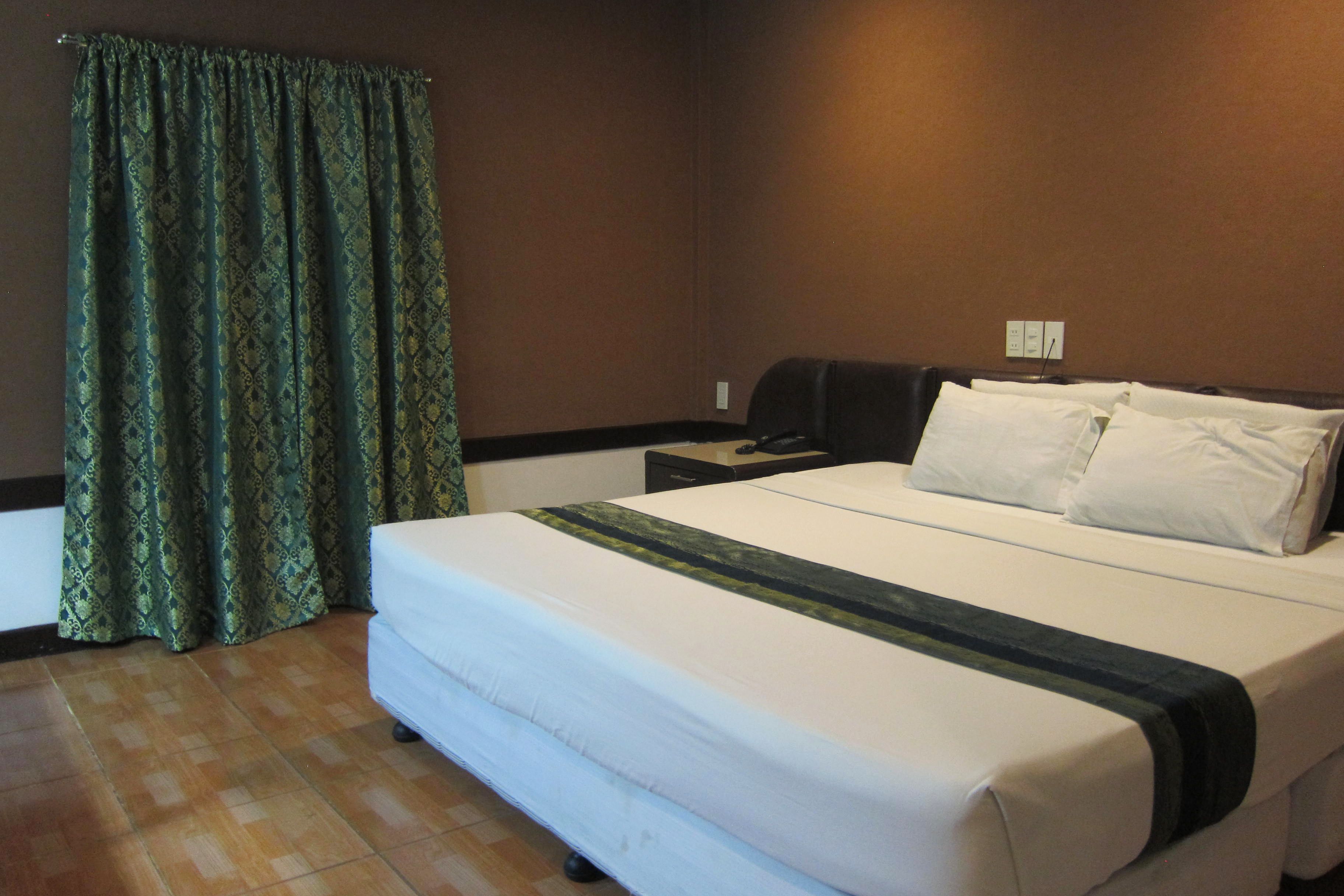 A hotel room with a large bed, a nightstand, a lamp, and a curtain.