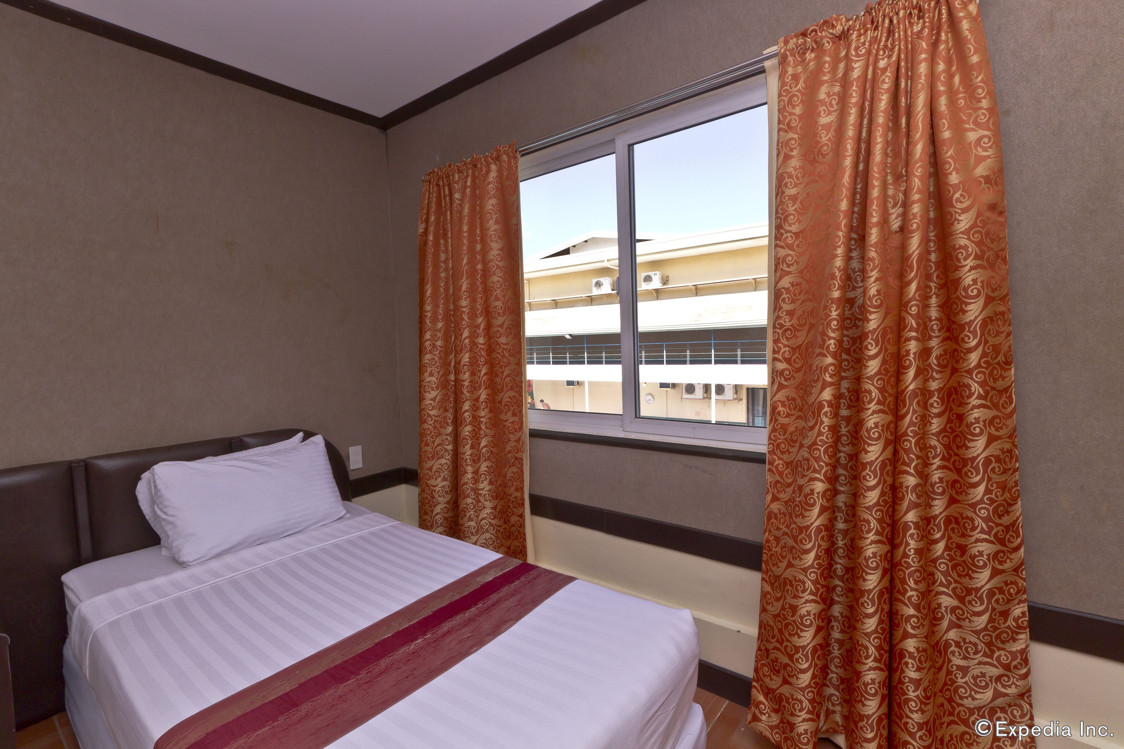 Habitación de hotel con cama, cortinas y ventana que da a un edificio.