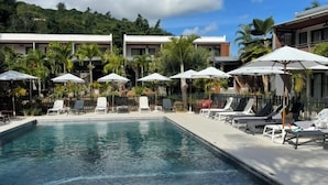 Una piscina con sillas de descanso y sombrillas, rodeada de edificios y palmeras.
