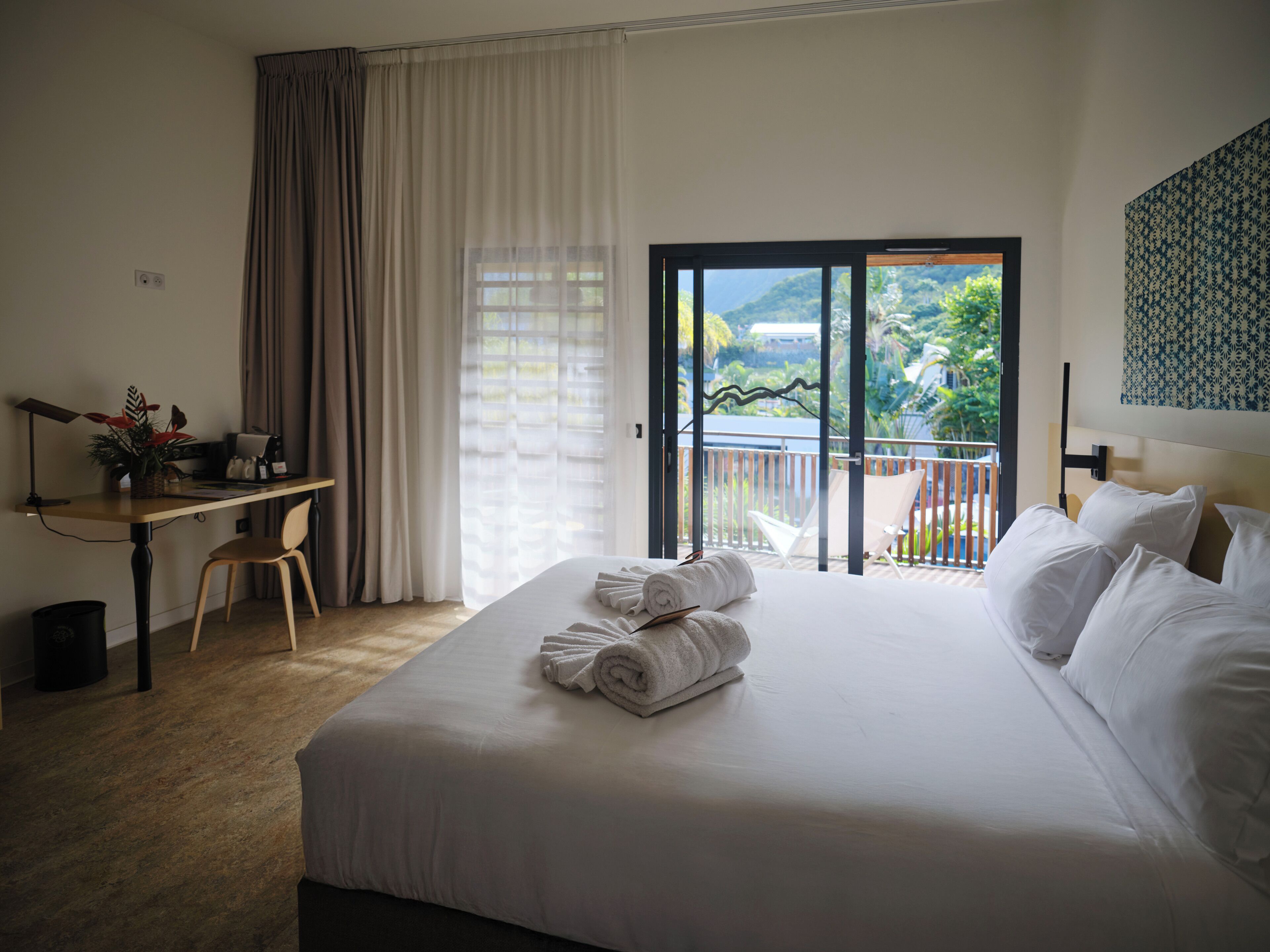 Ein Hotelzimmer mit Bett, Schreibtisch, Stuhl und einem Balkon mit Blick auf Grünflächen.