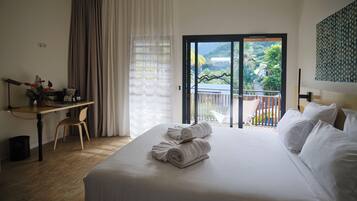 Ein Hotelzimmer mit Bett, Schreibtisch, Stuhl und einem Balkon mit Blick auf Grünflächen.