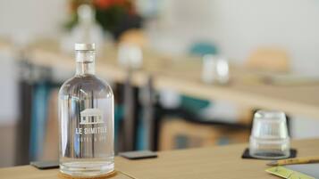 A clear bottle labeled "LE DIMITLE HOTEL & SPA" on a wooden table with a smartphone and a notepad.