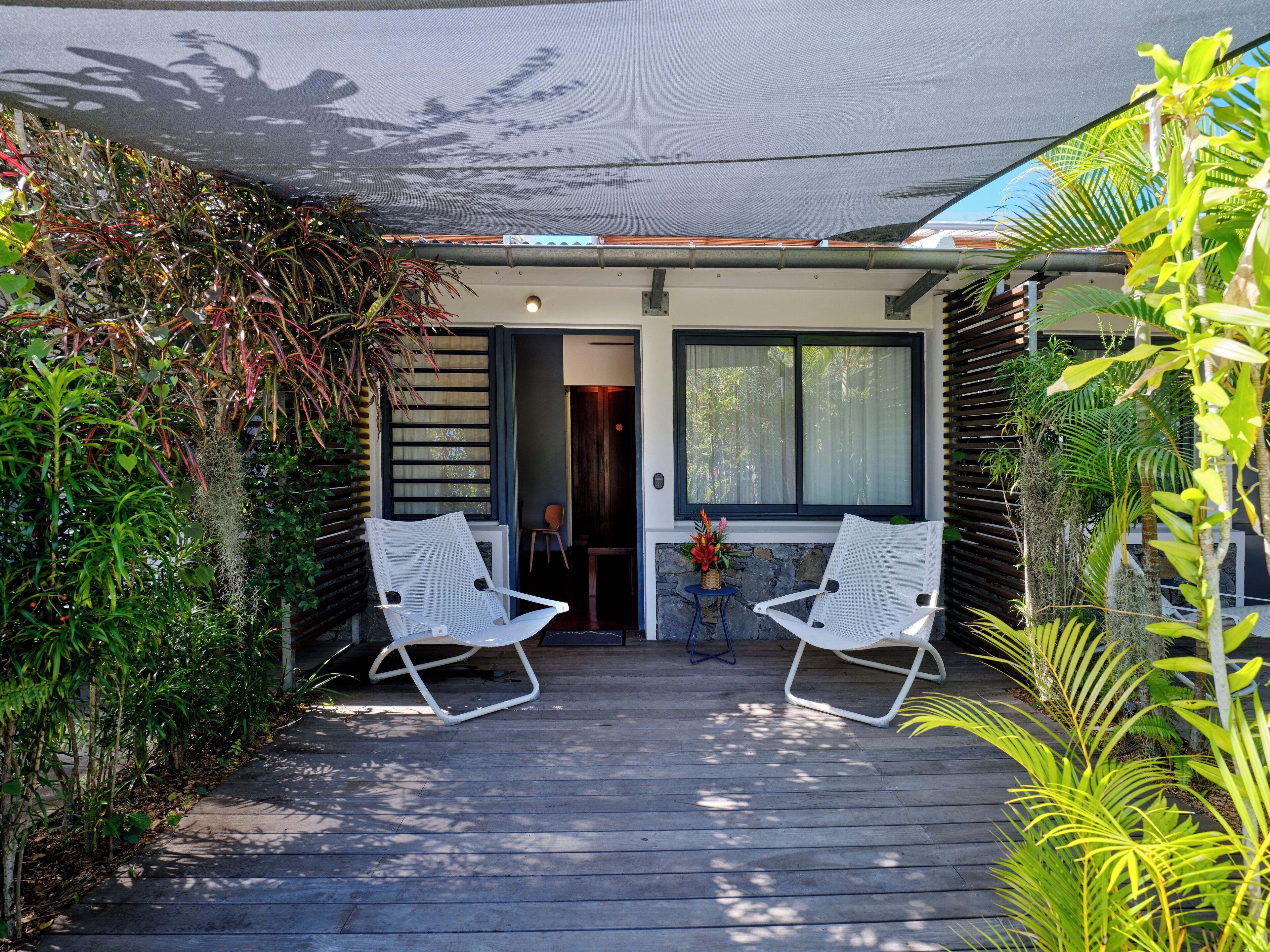 A covered outdoor area with two white chairs, a small table, and a potted plant.