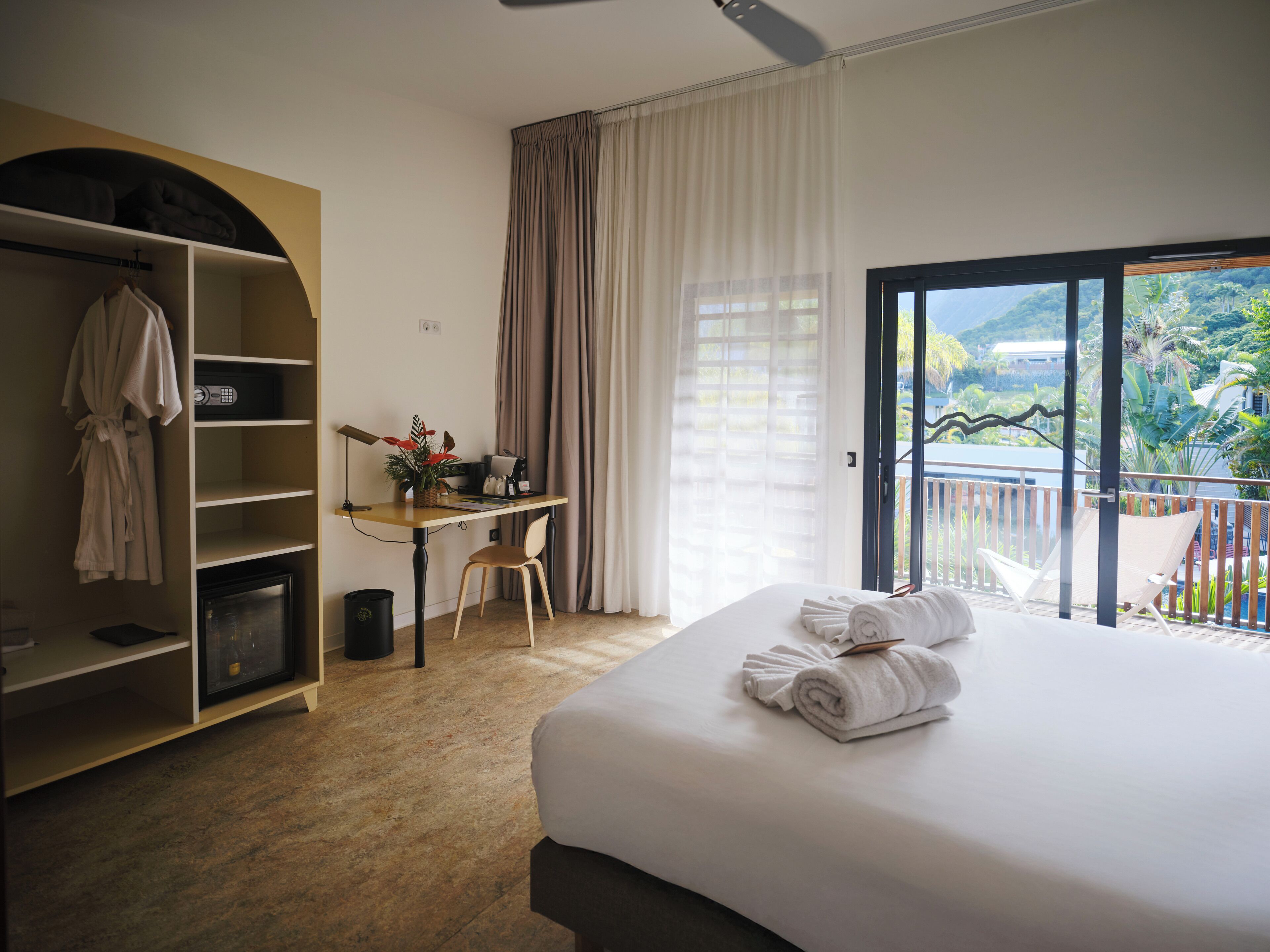 Habitación de hotel con cama, escritorio, silla, armario y balcón con vistas.