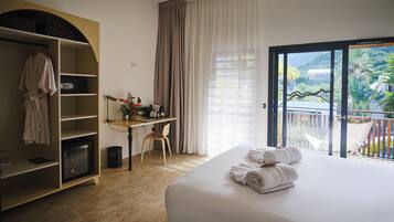 Habitación de hotel con cama, escritorio, silla, armario y balcón con vistas.