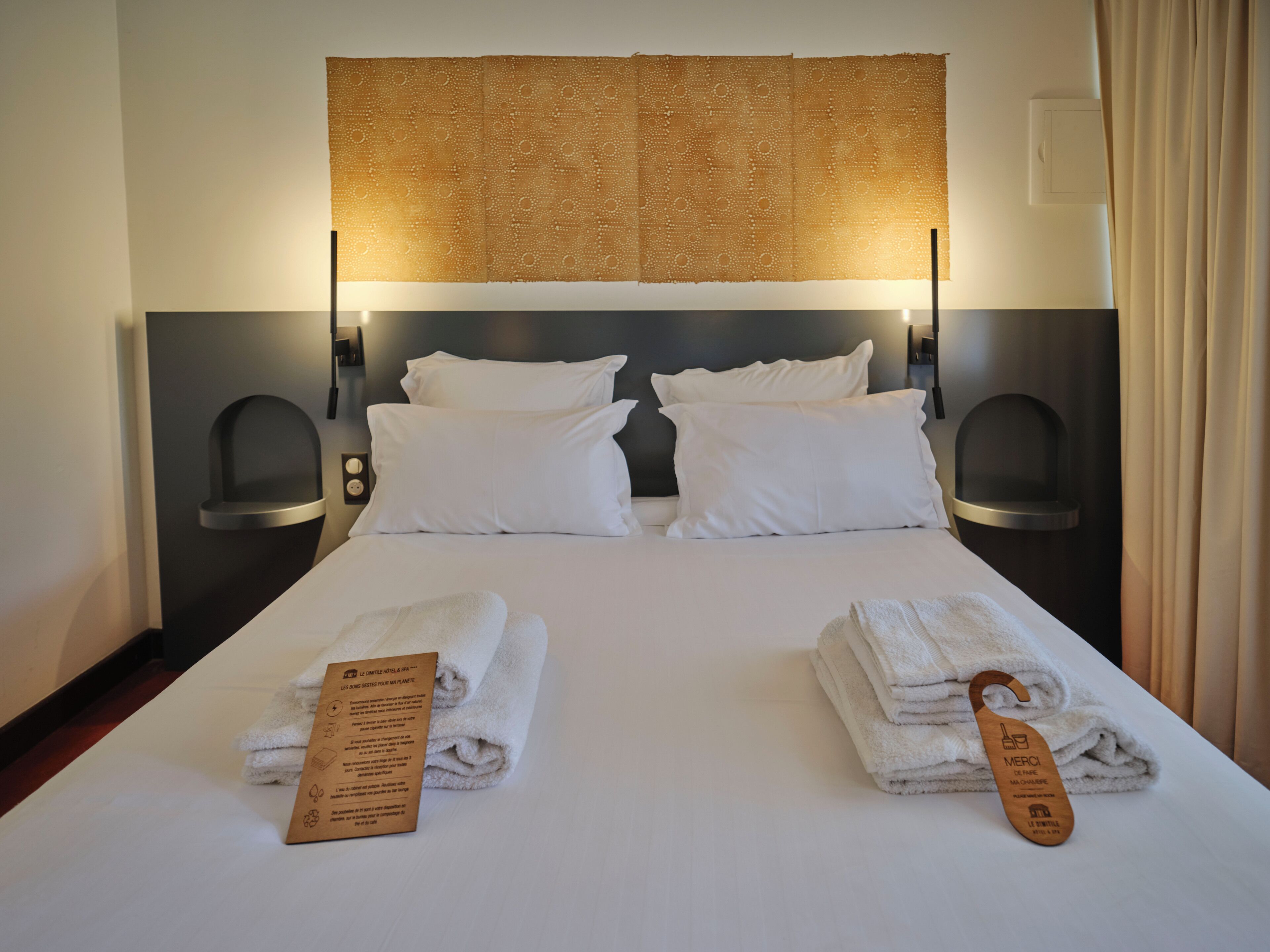 Een hotelkamer met een net opgemaakt bed, twee kussens, een hoofdbord met een patroon en twee wandlampen.