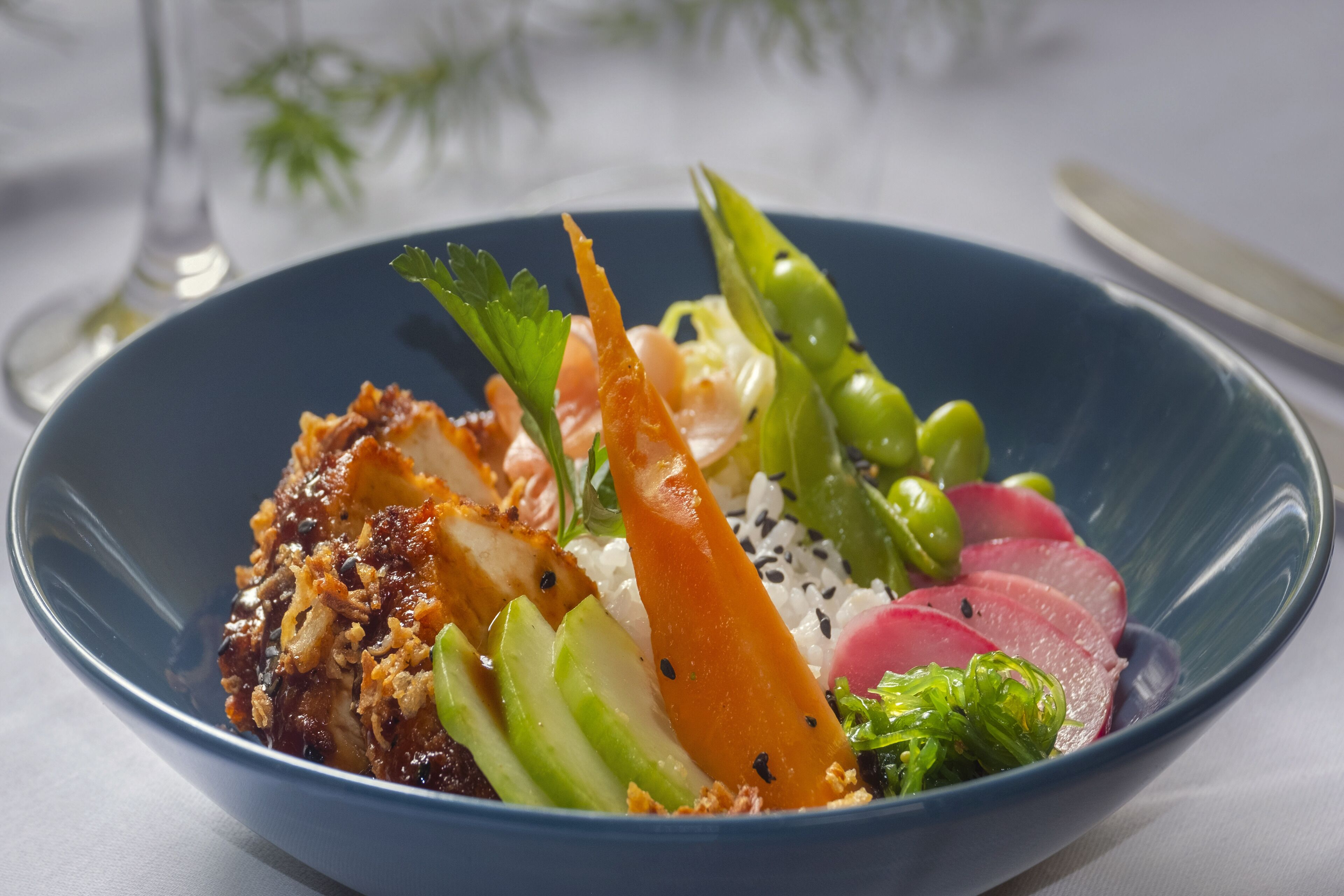 A blue bowl containing a variety of food items including sliced meat, vegetables, and rice.