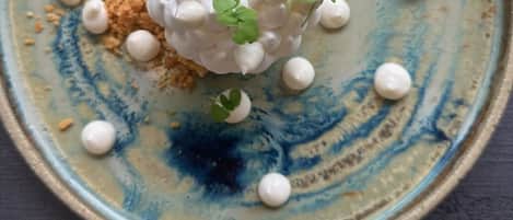Ein Teller mit einem kugelförmigen Dessert, garniert mit Minzblättern, auf einem blauen Keramikteller. Eine Löffel liegt daneben.