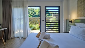 Habitación de hotel con cama, escritorio, silla y vista a un jardín por una puerta.