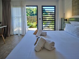 Habitación de hotel con cama, escritorio, silla y vista a un jard ín por una puerta.