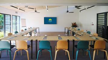 Une salle de conférence avec une longue table, des chaises, des ventilateurs de plafond et un écran fixé au mur qui affiche un logo.