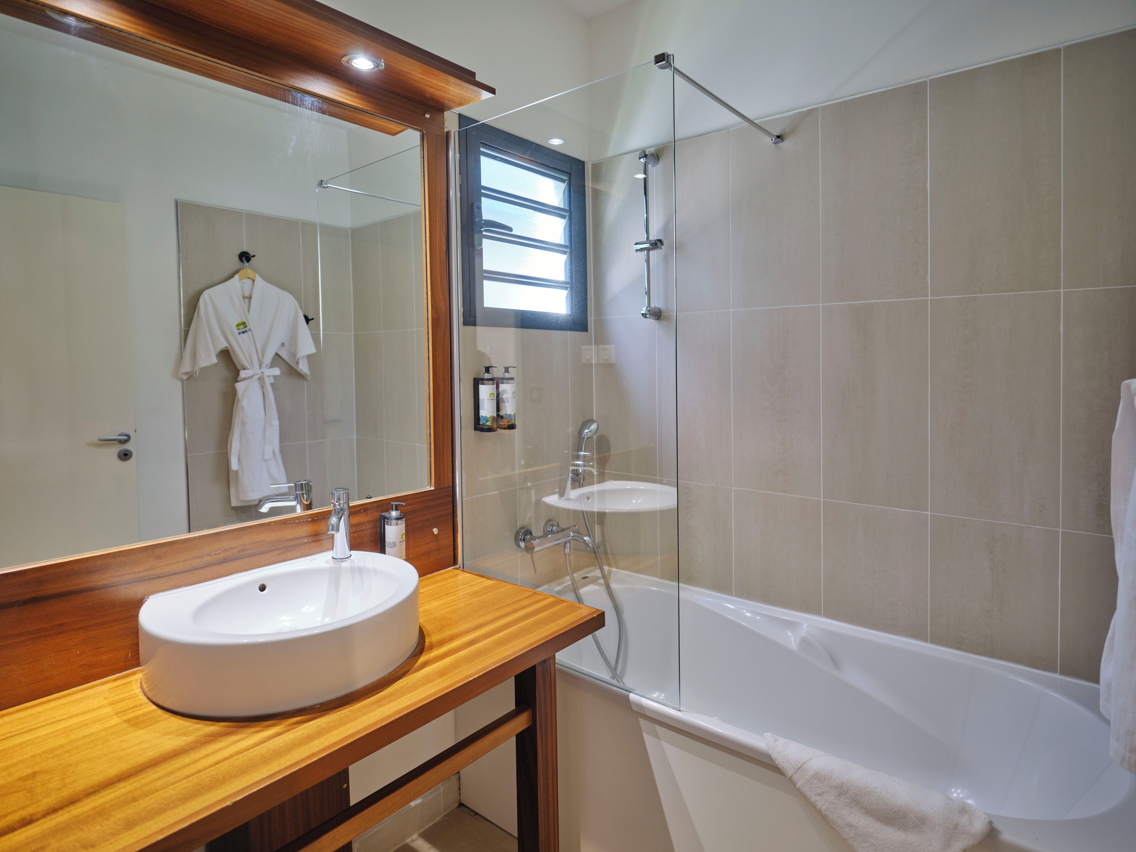 Ein Badezimmer mit einem Holzkosmetikschrank, einem großen Spiegel, einer Badewanne und einer Dusche.