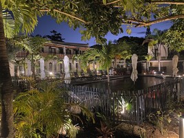 Vista nocturna de un patio de hotel con piscina, palmeras y zonas de estar al aire libre.