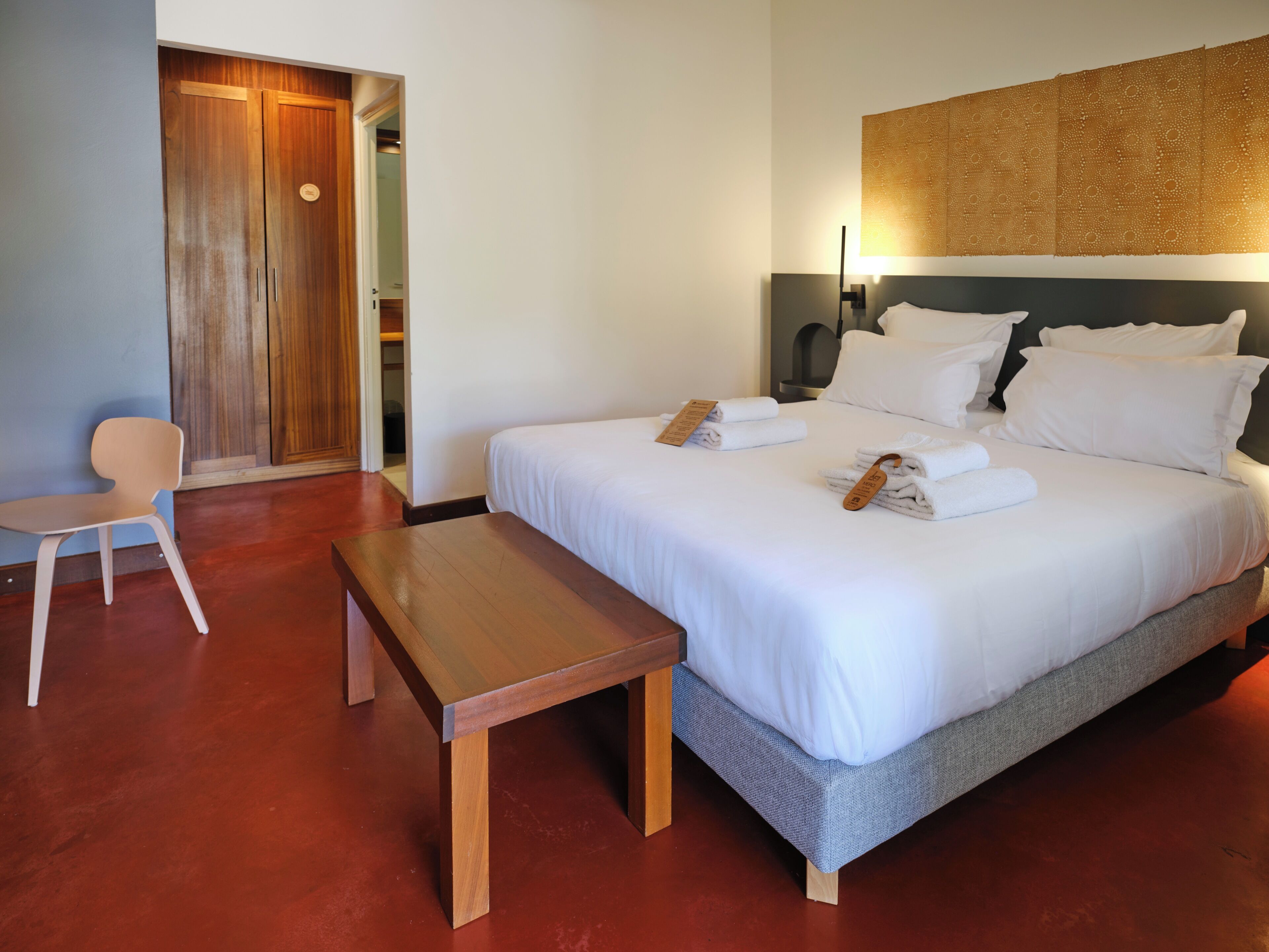 Une chambre d’hôtel comprenant un lit, une table de chevet, une chaise et une armoire en bois.