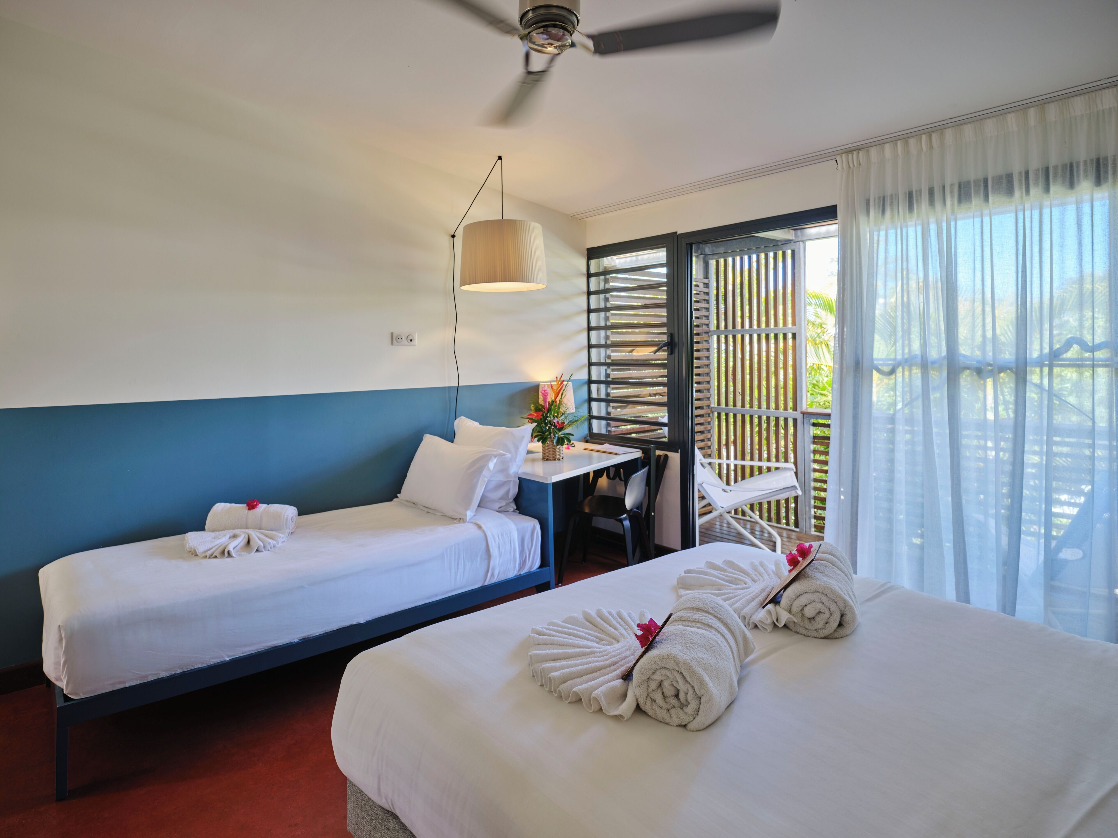 A hotel room with two beds, a desk, a chair, and a large window with a view.