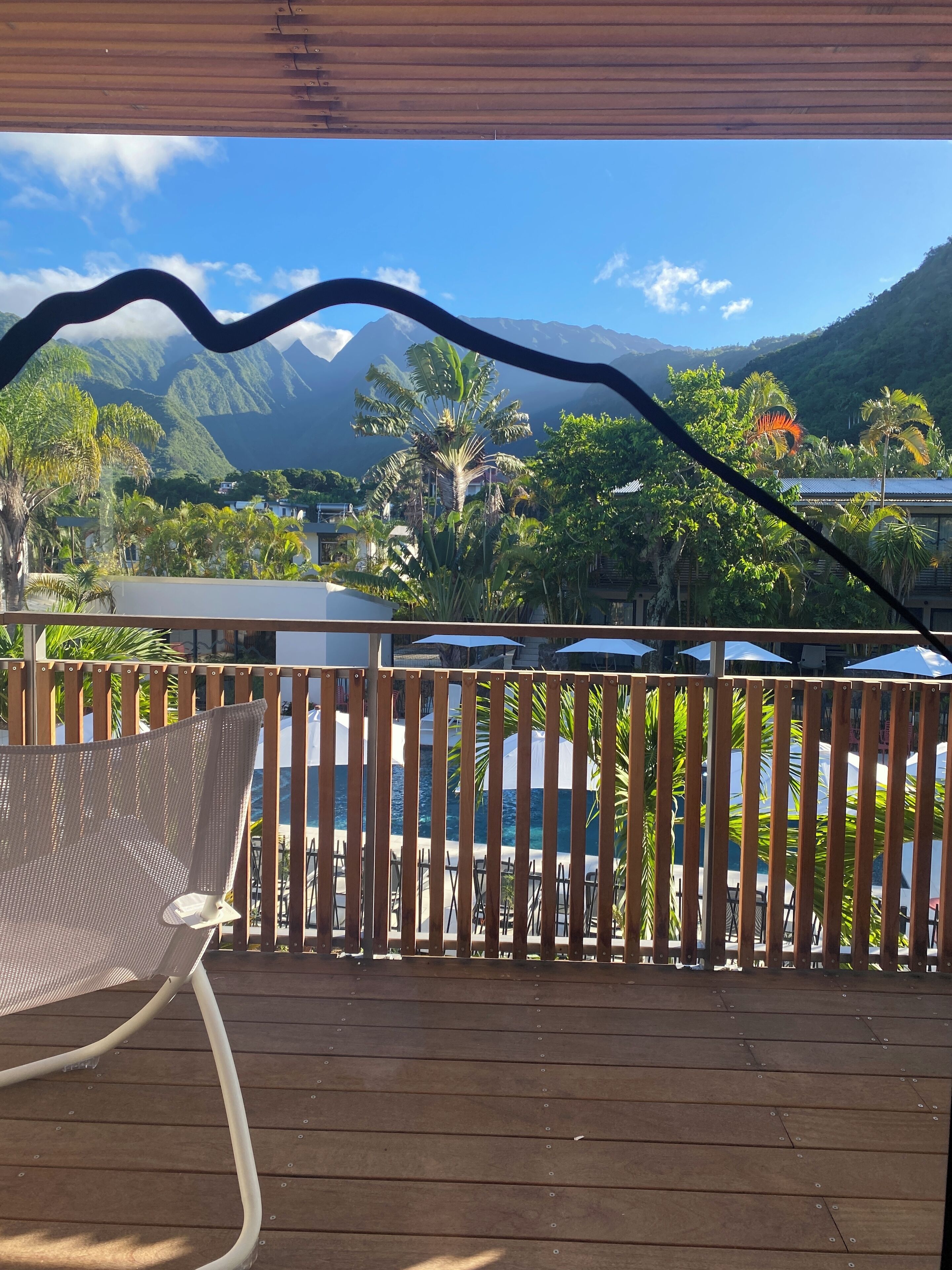 Eine Holzterrasse mit einem Metallstuhl und einem Pool im Hintergrund.