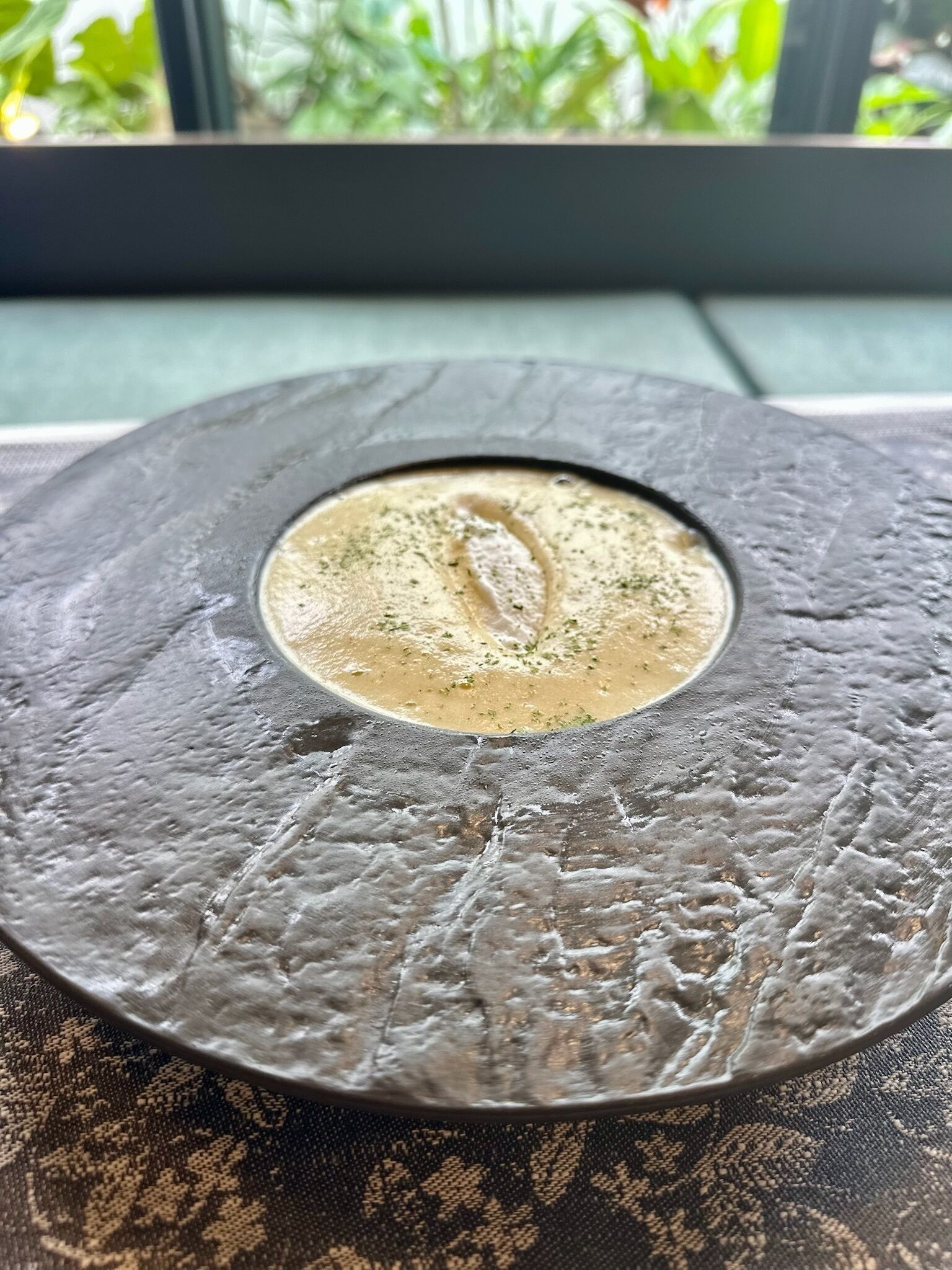 Una mesa redonda de piedra con textura y un recipiente poco profundo en el centro, que contiene un plato cremoso coronado con hierbas.