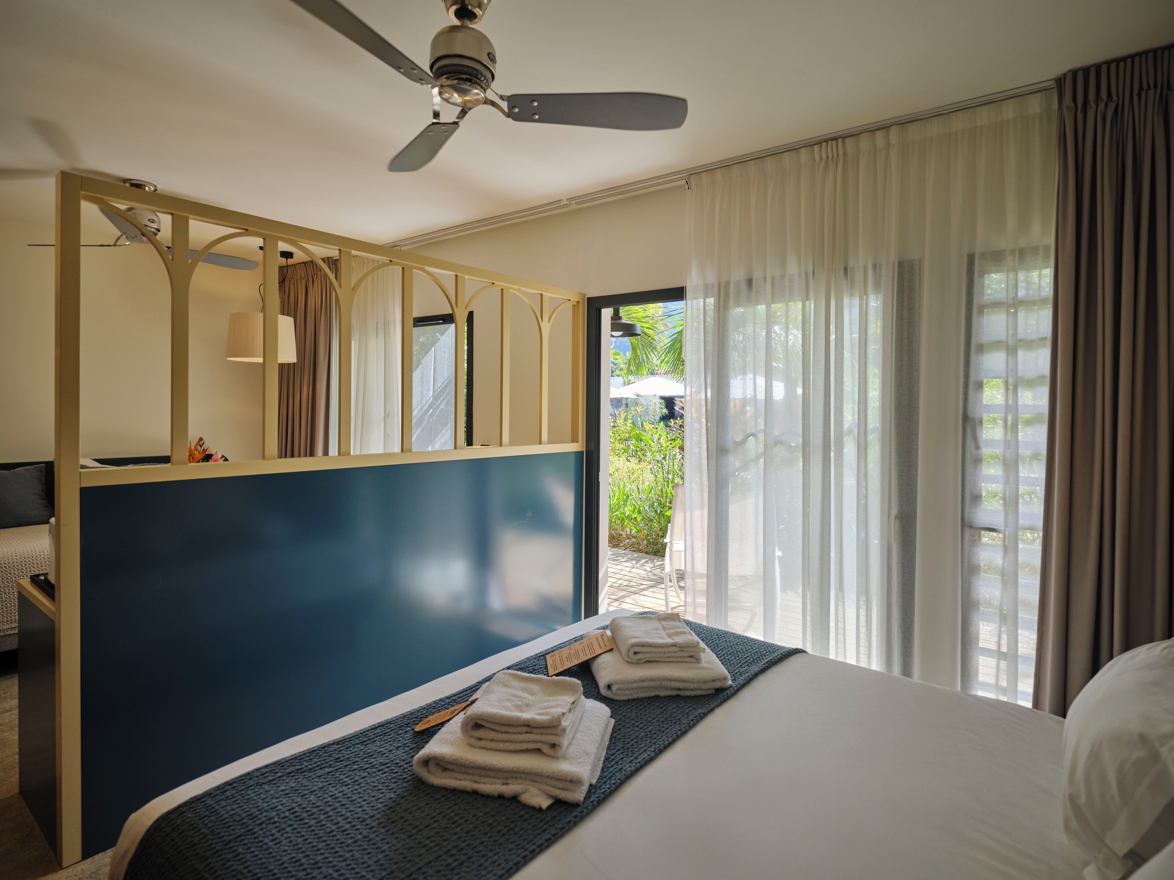 A hotel room with a bed, a desk, a ceiling fan, and a view of the outdoors.