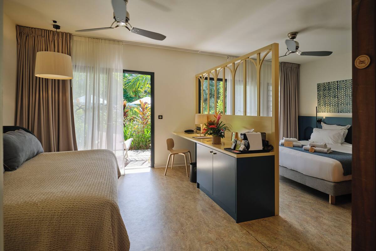 Quarto de hotel com cama, escrivaninha, cadeira, espelho e vista para o exterior.