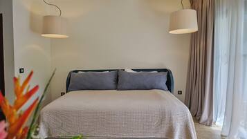 A bedroom with a bed, two pendant lights, a window with curtains, and a plant in the foreground.