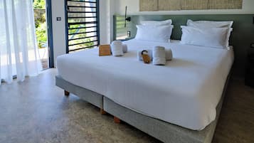 A modern hotel room with a large bed, white linens, and a view of greenery through the door.