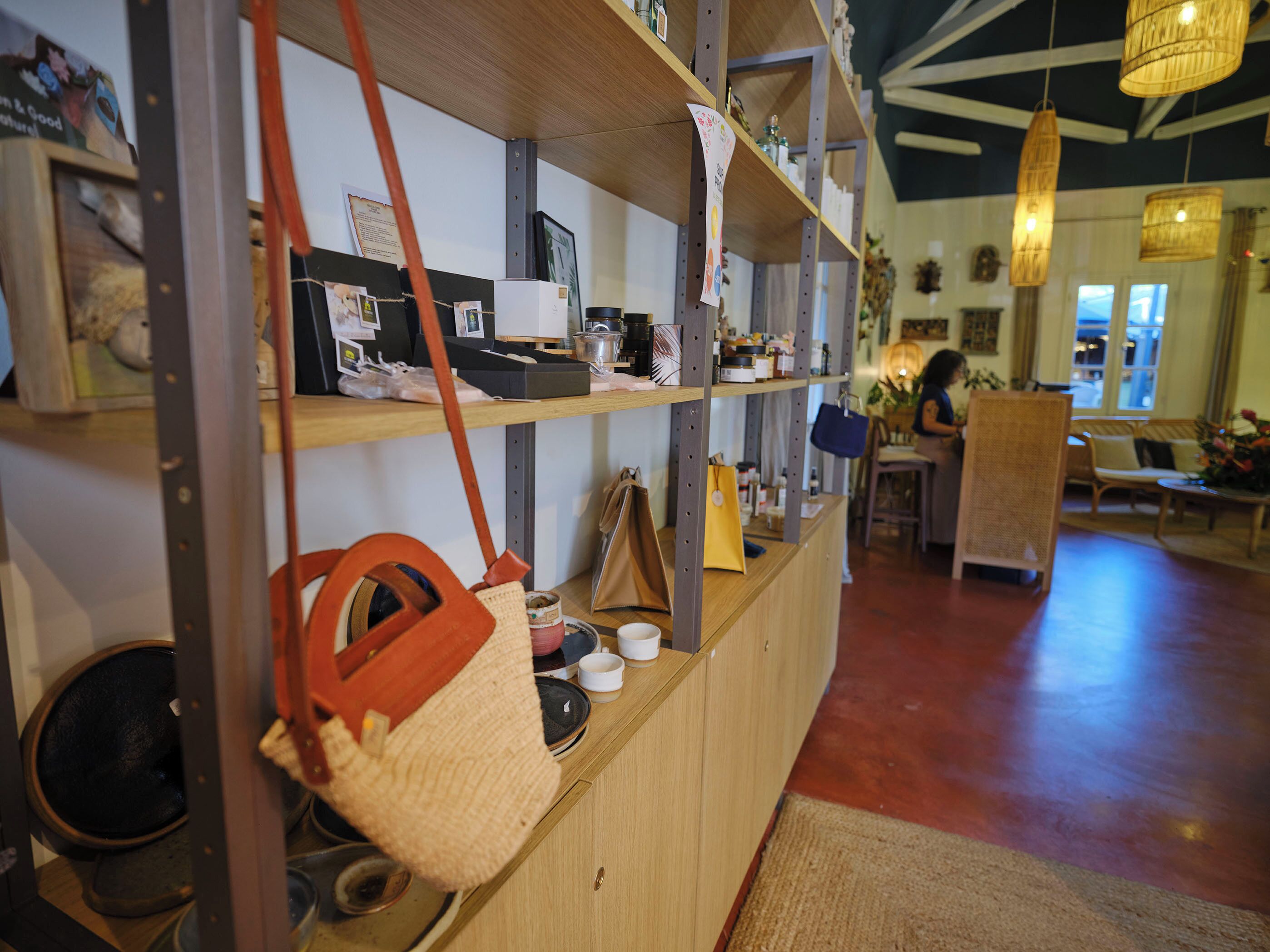 Interior de una tienda con estantes llenos de diferentes artículos, un mostrador con una cesta y una zona de estar al fondo.