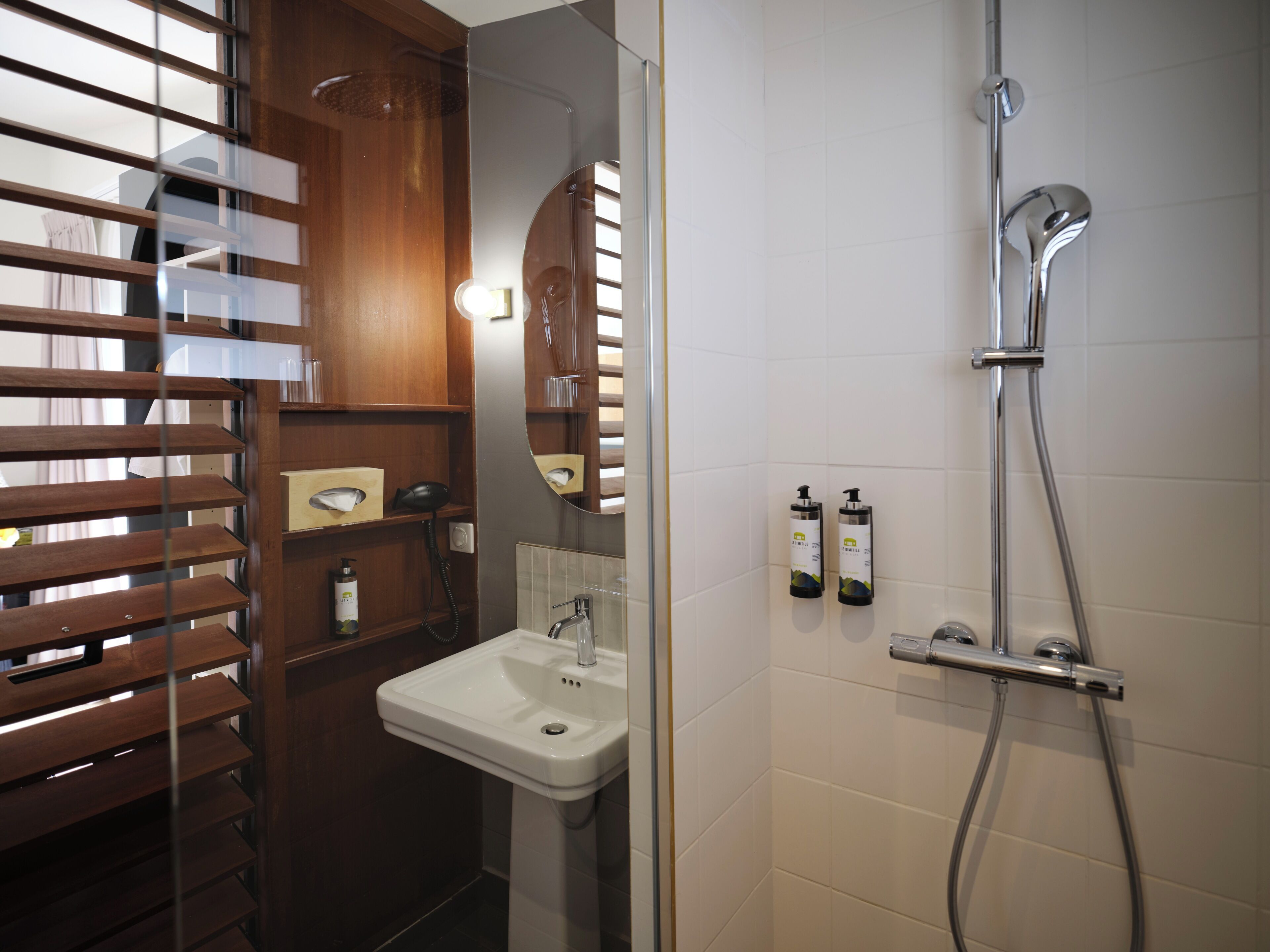 Un baño moderno con un mueble tocador de madera, un lavabo blanco y una ducha con cabezal de ducha manual.