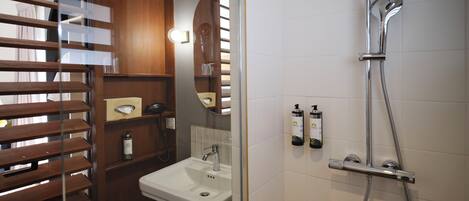 Un baño moderno con un mueble tocador de madera, un lavabo blanco y una ducha con cabezal de ducha manual.
