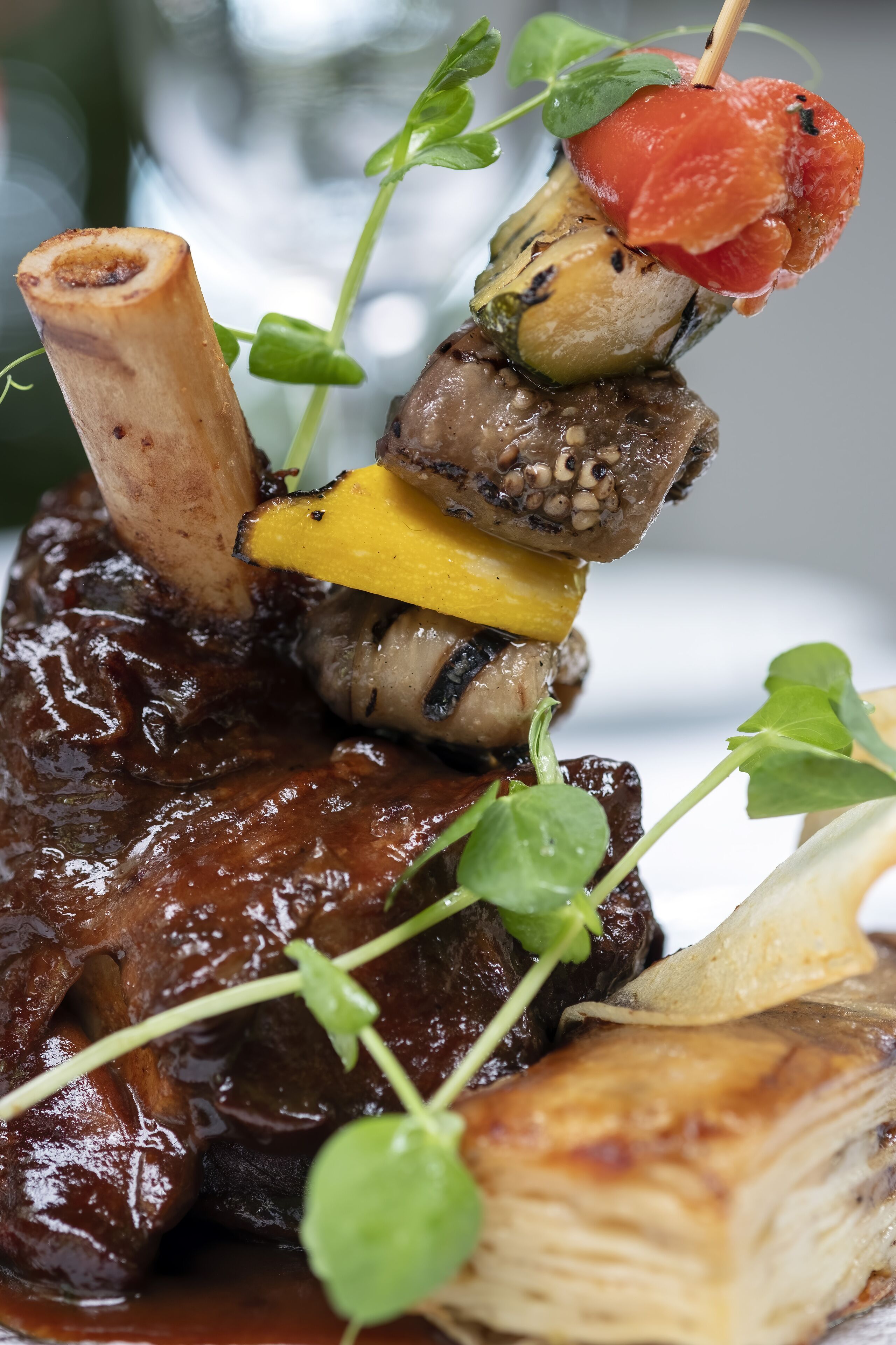 A dish with a bone, mushrooms, and a slice of tomato on a skewer, garnished with greens.