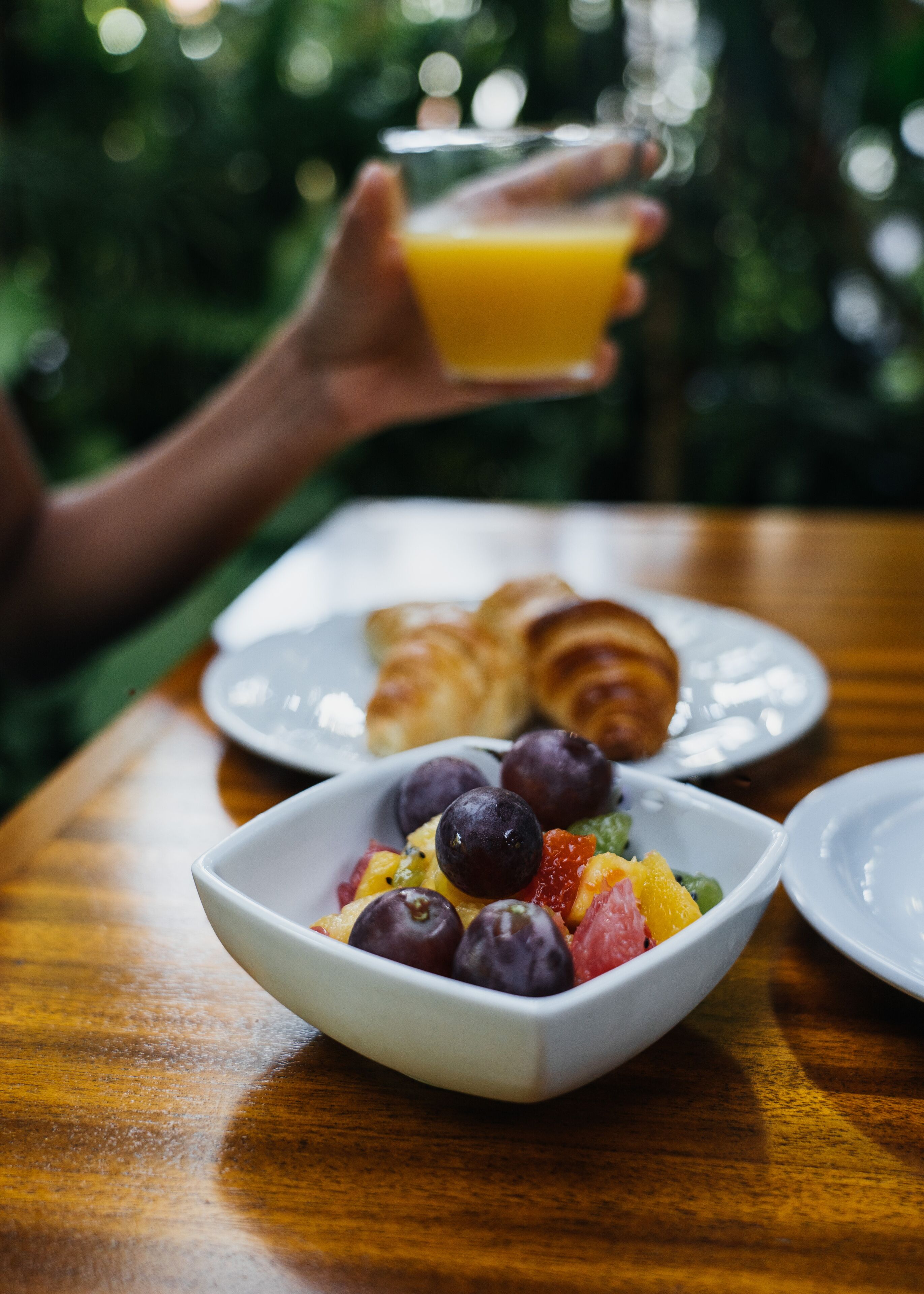 Une table en bois dressée pour le petit-déjeuner, avec des croissants, un bol de fruits et un verre de jus d’orange.