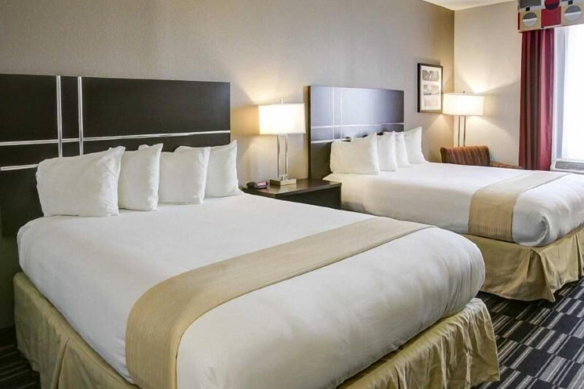 Ett hotellrum med två sängar, en sänggavel, sänglampor, en inramad tavla och ett fönster med gardiner.