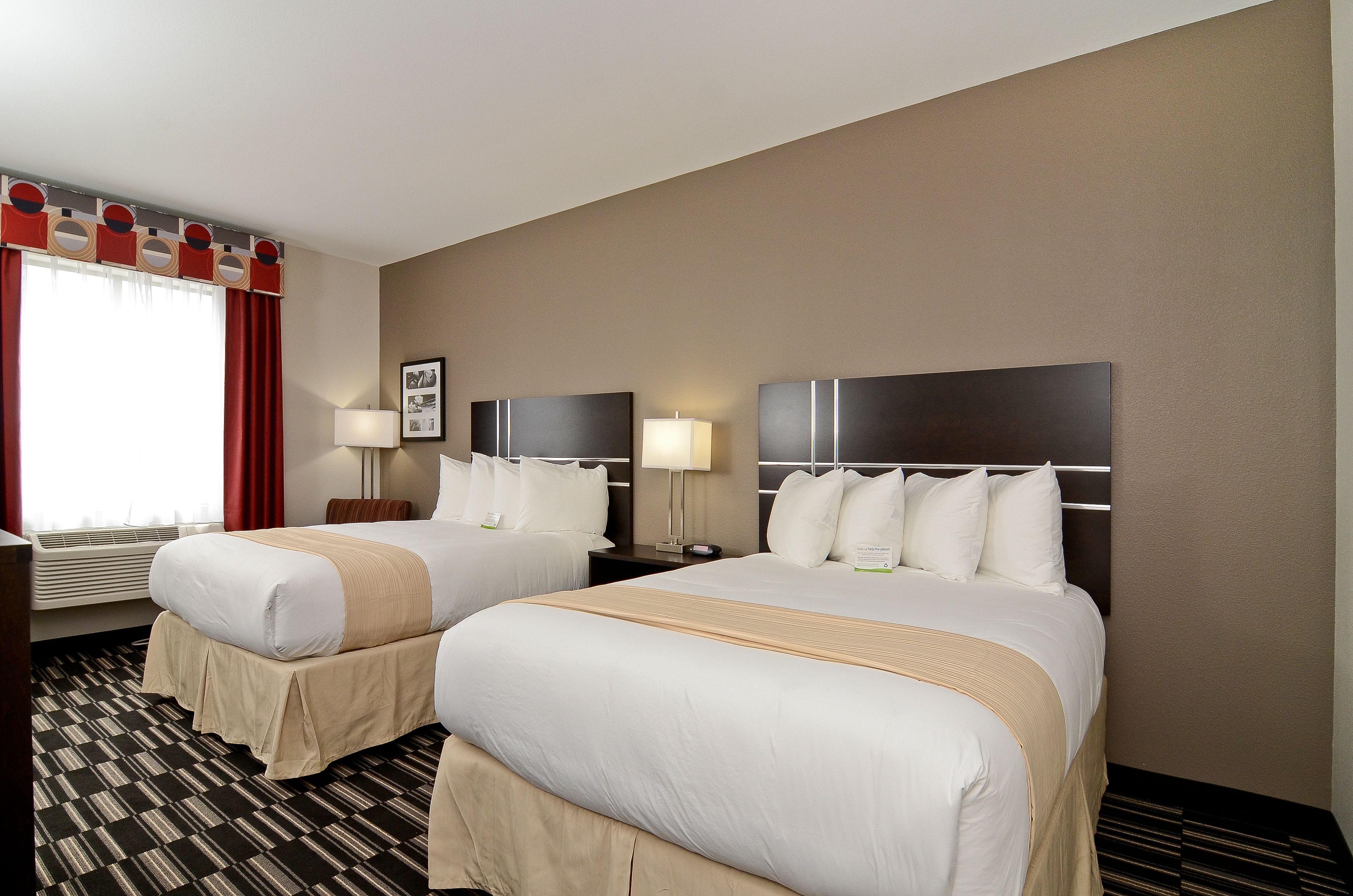 Habitación de hotel con dos camas, un ventanal grande con cortinas rojas, un televisor montado en la pared y una mesita de noche con lámpara.