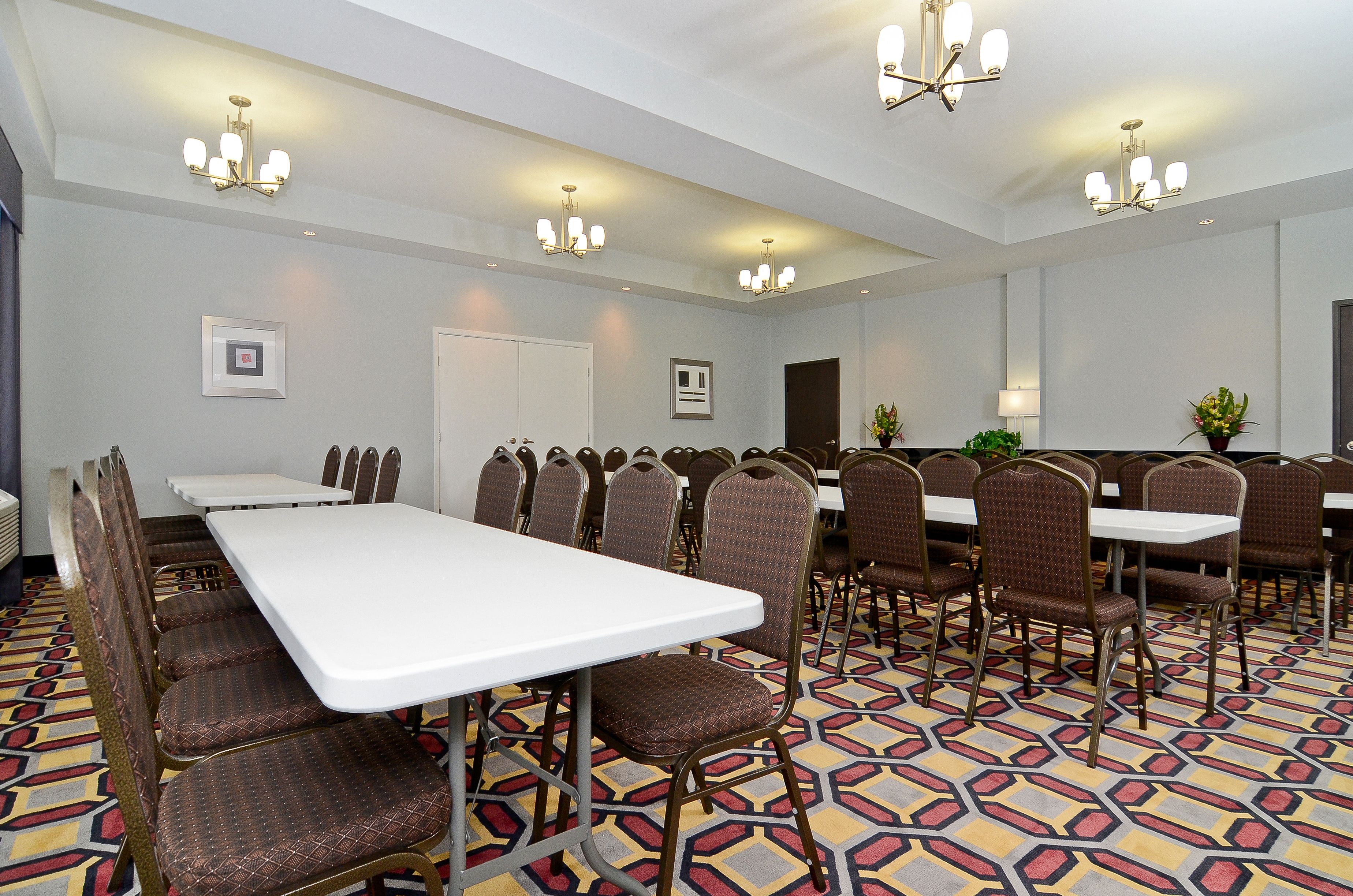 A conference room with white tables and brown chairs, patterned carpet, and chandeliers.