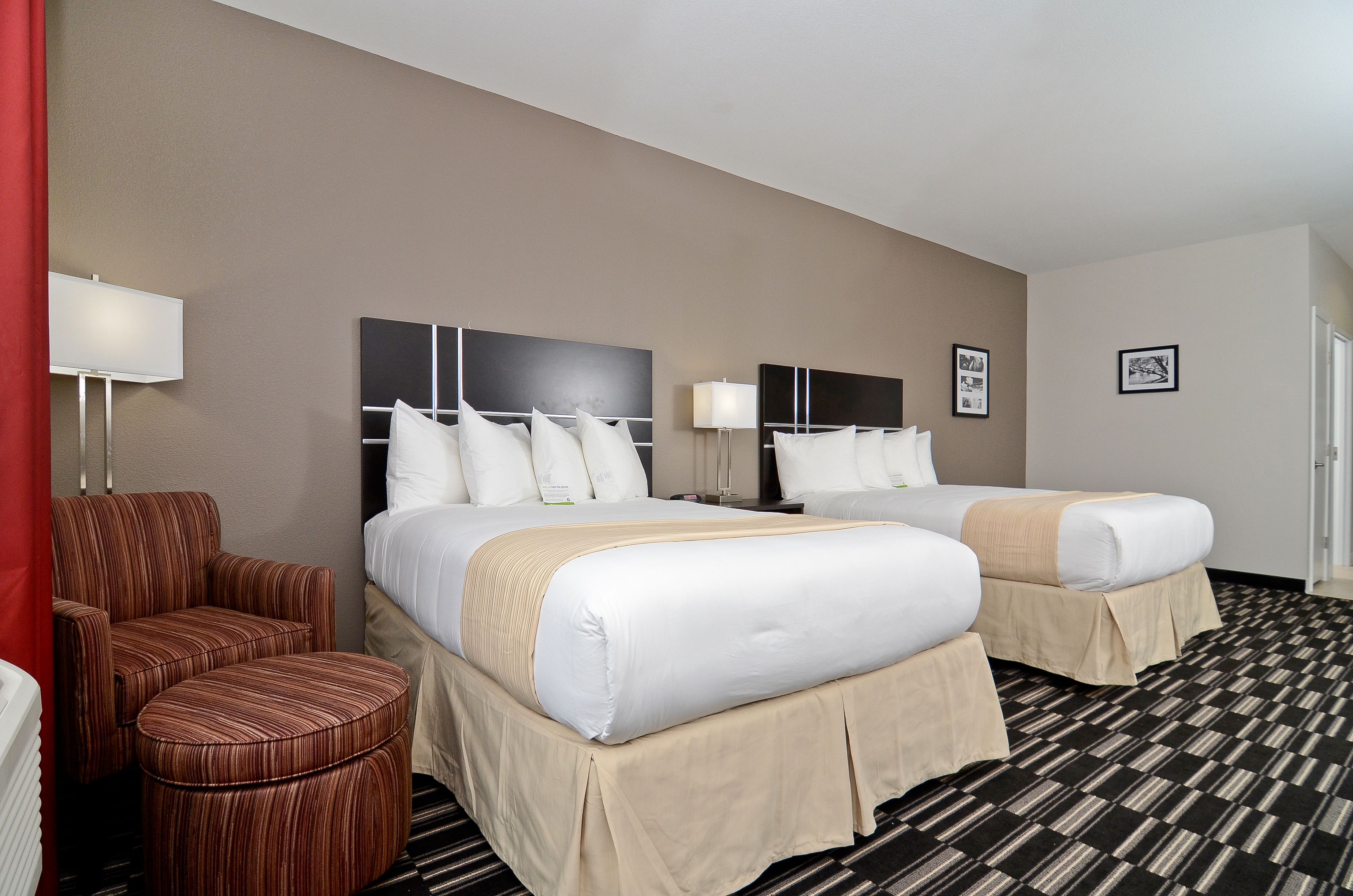 A hotel room with two beds, a chair, and a red curtain.