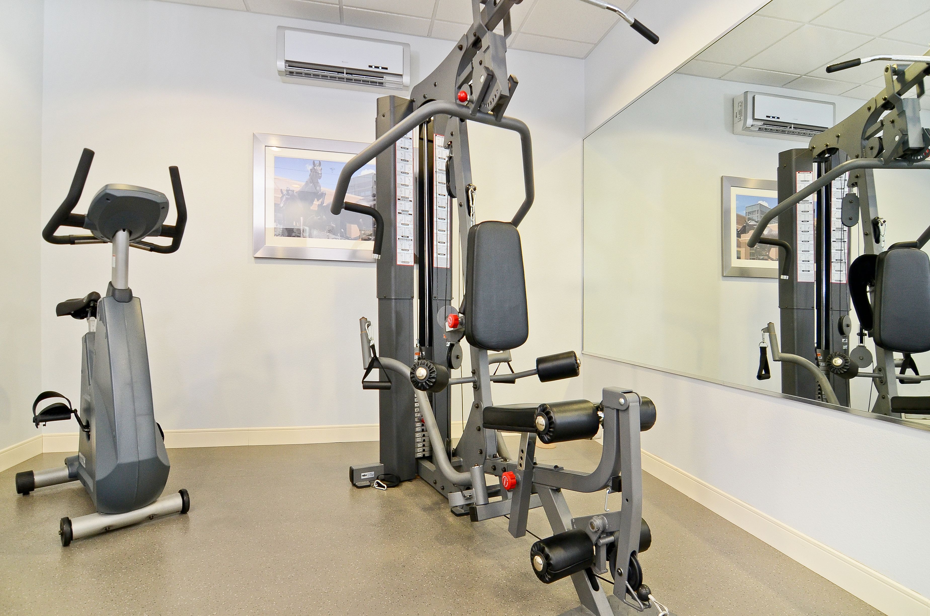 Un gimnasio con equipo de ejercicio, un espejo y cuadros en la pared.