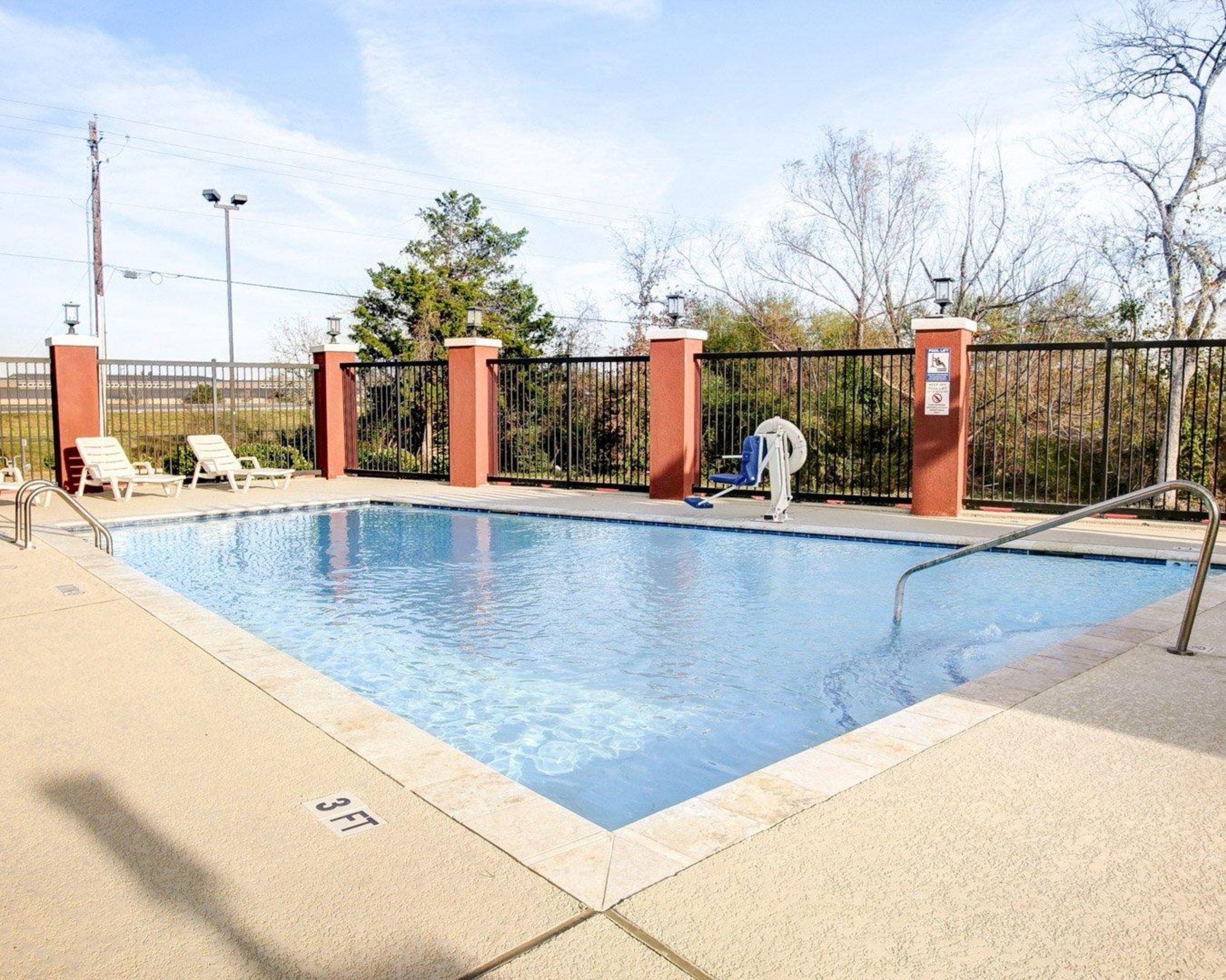 A swimming pool with a 3ft depth marker, surrounded by a fence and lounge chairs.