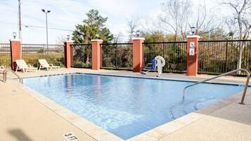 A swimming pool with a 3ft depth marker, surrounded by a fence and lounge chairs.