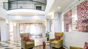 A spacious lobby with a checkered floor, two armchairs with red cushions, a glass coffee table, and a decorative wall with geometric patterns.