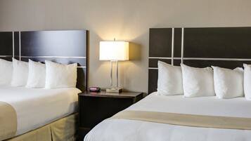 Una habitación de hotel con dos camas, una mesita de noche con lámpara y un reloj digital.