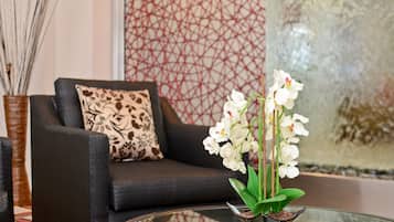 Una sala de estar moderna con un sofá negro, un cojín estampado y una mesa de centro de vidrio con orquídeas blancas.