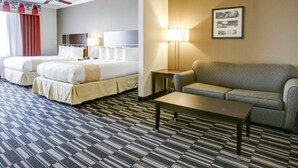 A hotel room with two beds, a sofa, a coffee table, a lamp, and a ceiling fan.