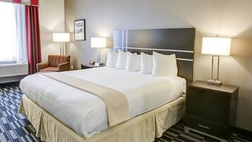 A hotel room with a large bed, two bedside tables with lamps, a chair, a window with curtains, and a framed picture on the wall.