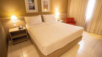 A hotel room with a large bed, two bedside lamps, a nightstand with a phone, a small table, and a red chair.