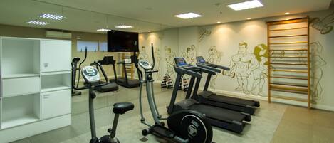 A gym with cardio machines, weight benches, and a wall mural.