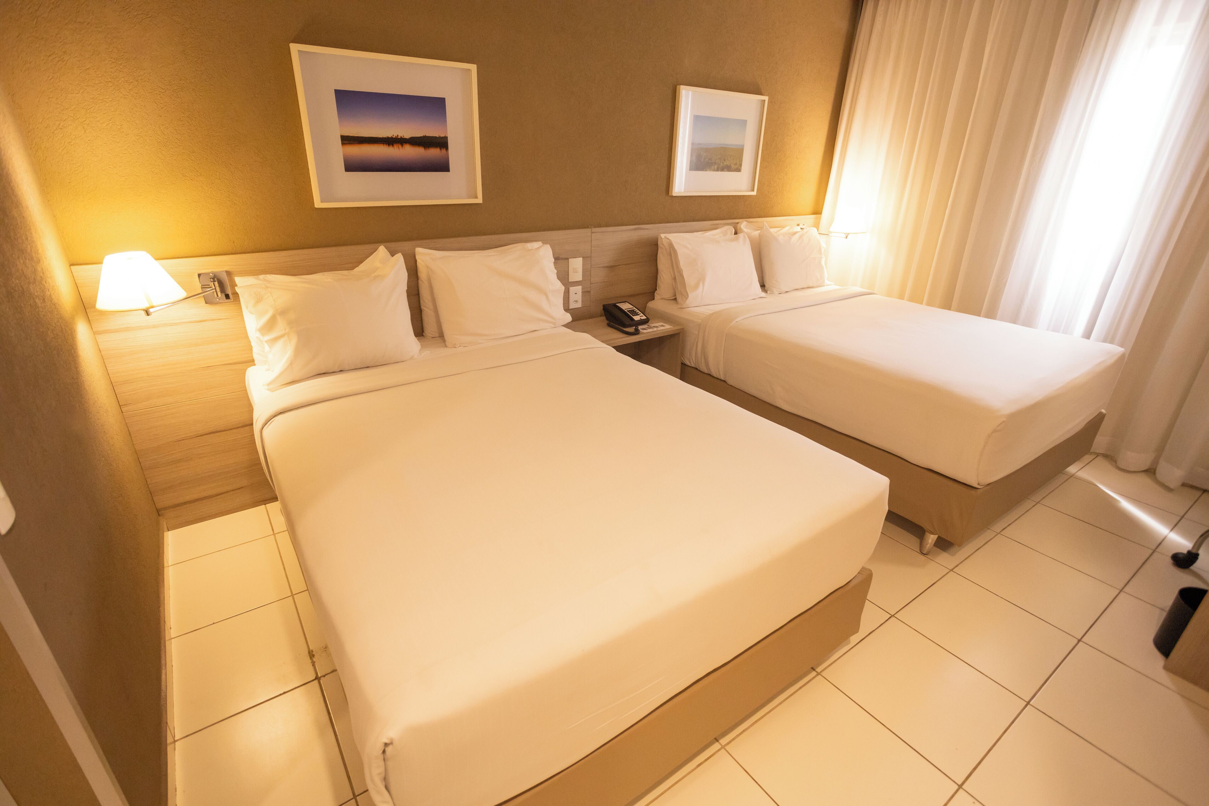 A hotel room with two beds, a nightstand with a phone, and two framed pictures on the wall.