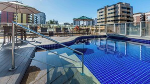 A rooftop pool with blue tiles, lounge chairs, and umbrellas.
