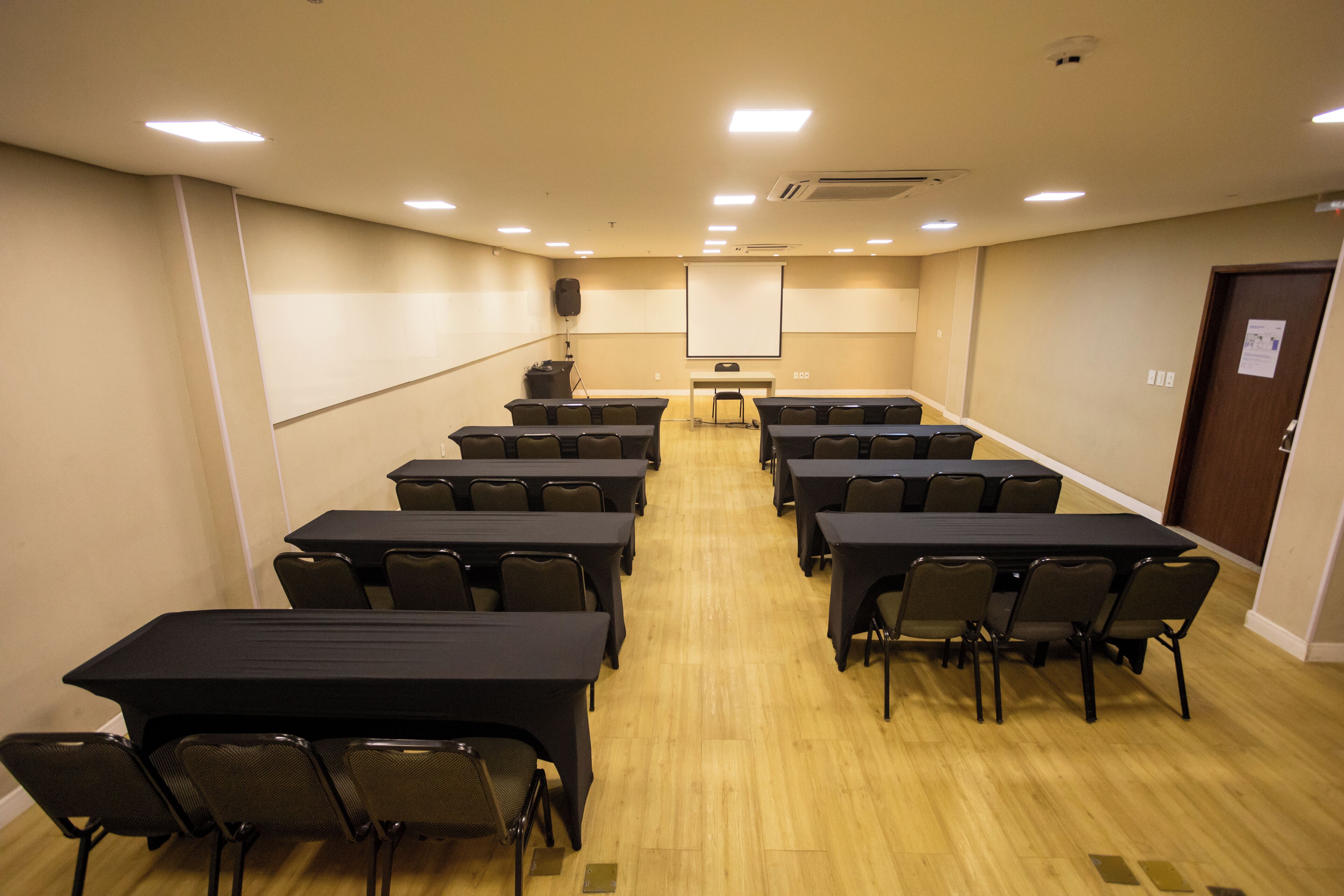 A conference room with multiple tables and chairs, a projector screen, and a podium.
