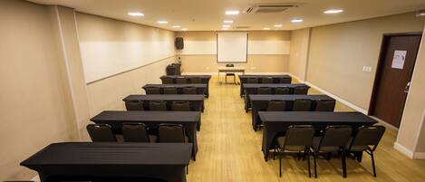 A conference room with multiple tables and chairs, a projector screen, and a podium.
