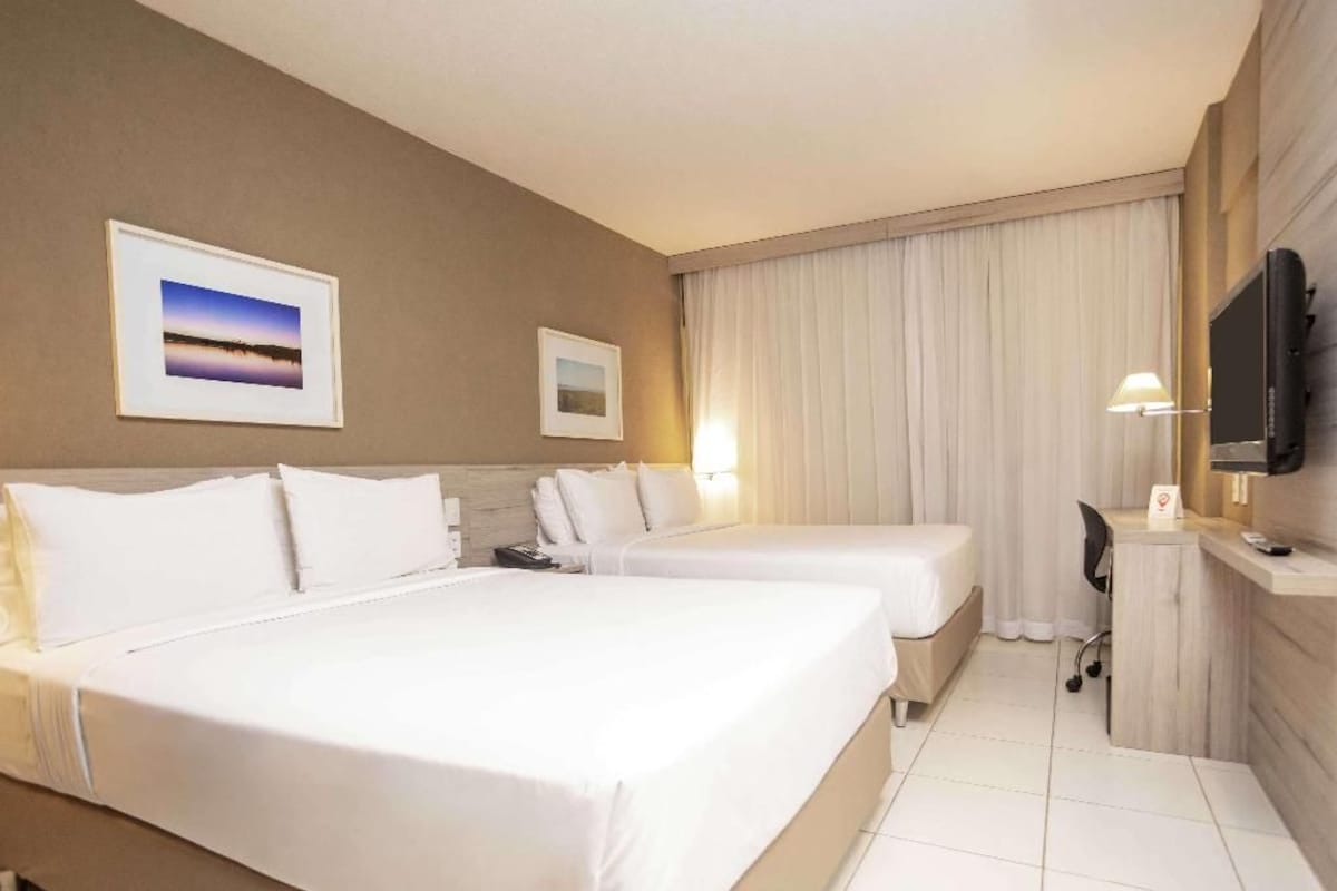 A hotel room with two beds, a desk, a television, and artwork on the walls.